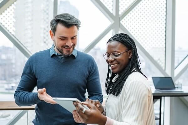 Two colleagues pass a tablet between them in a bright office.