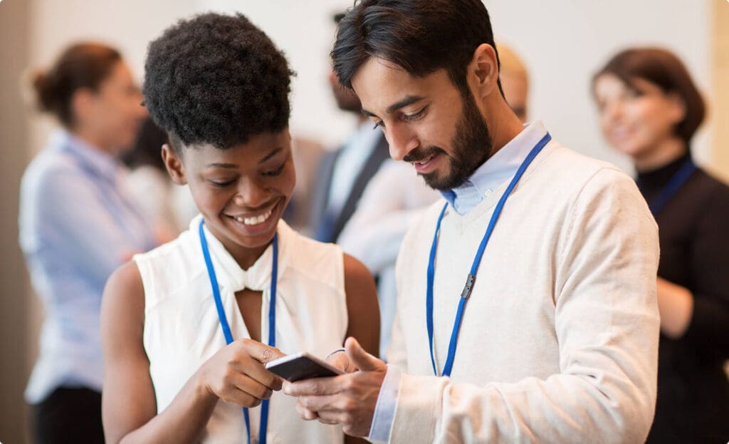 Woman and man smiling while analyzing data in a smartphone at an event.