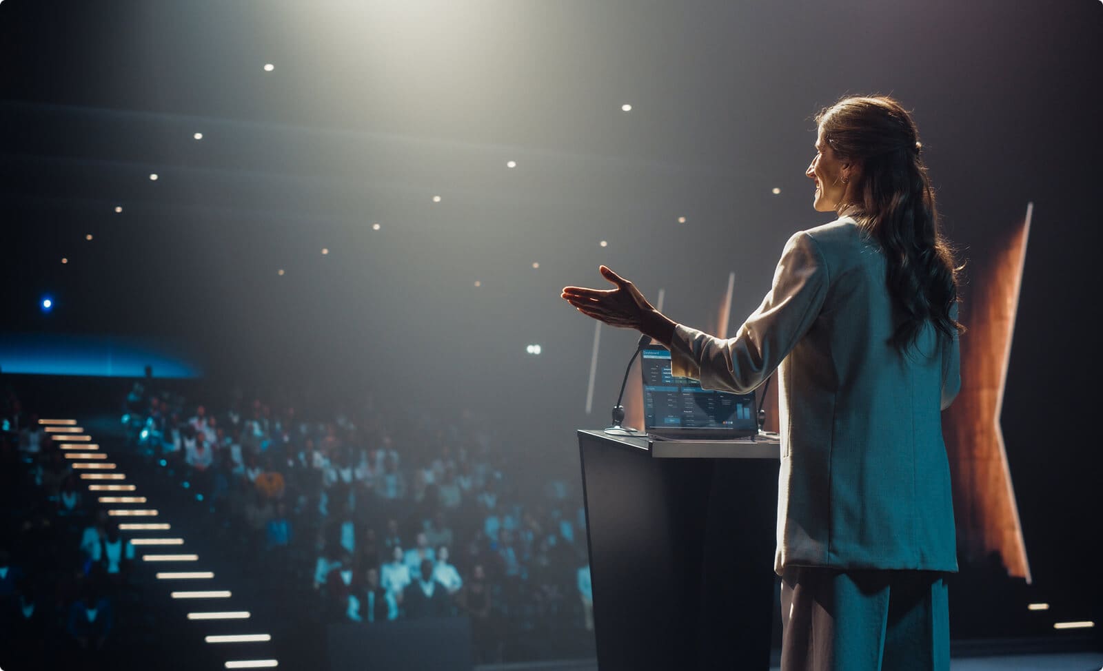 Businesswoman speaking on podium at a conference. Photo facing the crowd from behind the speaker.