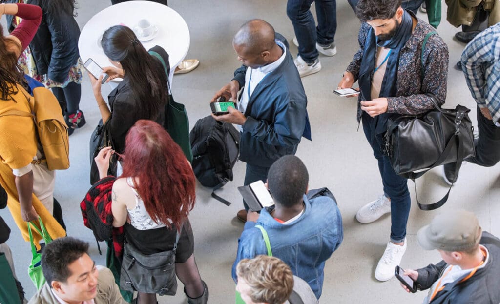 People standing in line at an event while some look at their mobile phones.